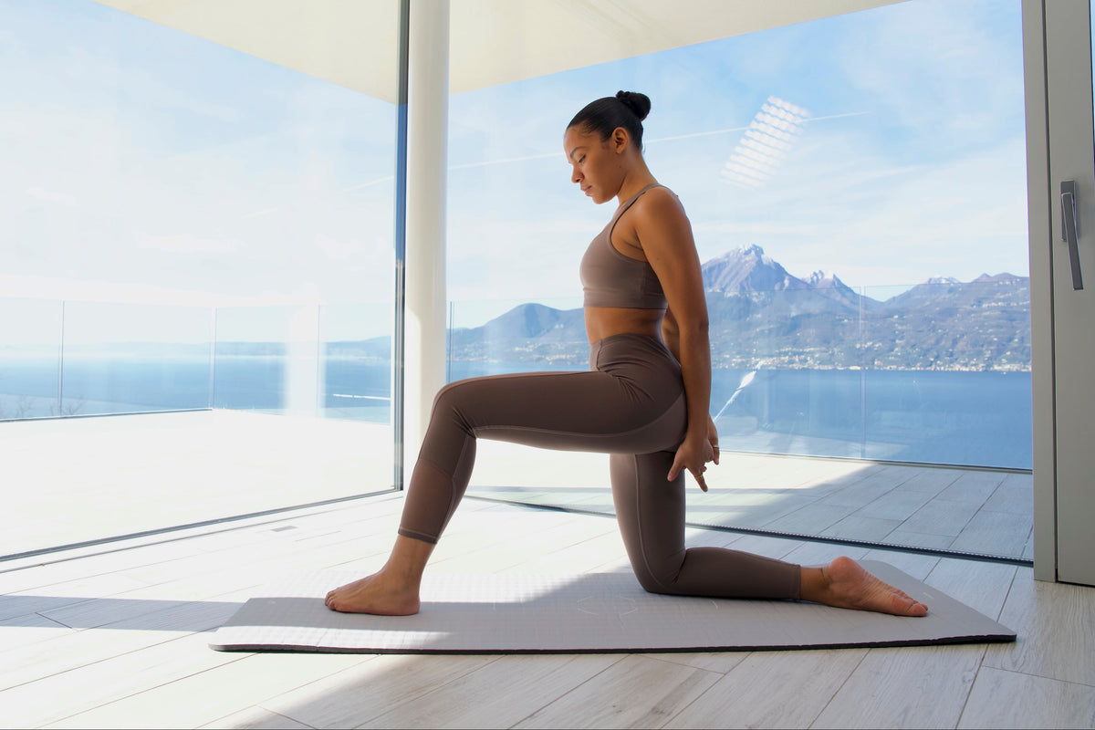 A woman stretching on a mat in a bright room overlooking a lake and mountains