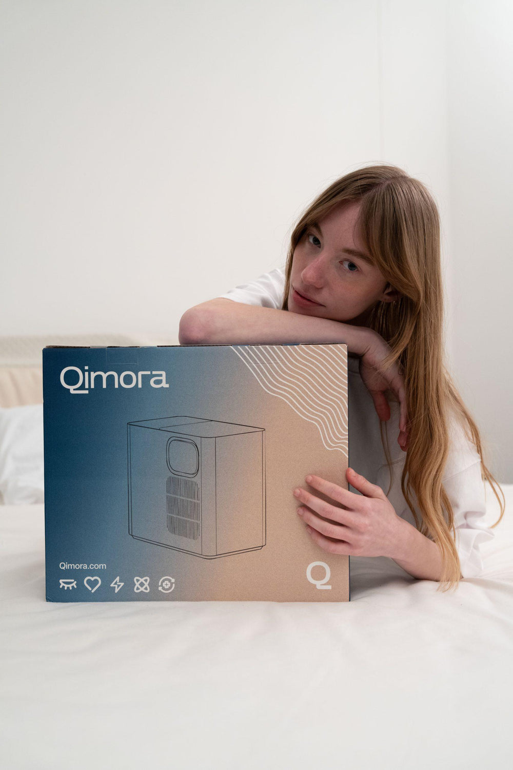 A woman in bed leaning on the Qimora Sleep Core box